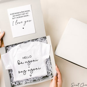 May include: A white baby onesie with the text "HELLO bà ngoại + ông ngoại" inside a grey gift box. A card with the text "HI BÀ NGOẠI & ÔNG NGOẠI, WE HAVEN'T MET YET BUT I ALREADY KNOW... I love you" is also in the box.