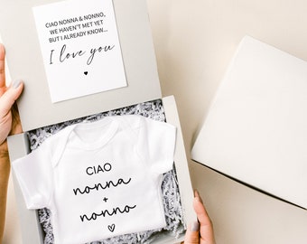 May include: A white baby onesie with the text "CIAO nonna + nonno" and a small heart. The onesie is in a white gift box with white tissue paper. A card with the text "CIAO NONNA & NONNO, WE HAVEN'T MET YET BUT I ALREADY KNOW... I love you" is visible in the background.