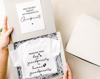 May include: A white onesie with black text that reads "Promoted from dog grandparents to human grandparents" in a gift box with white tissue paper. A card with the text "Only the best parents get promoted to grandparents" is also in the box.