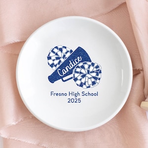 May include: White ceramic trinket dish with a blue and white cheerleading megaphone and pom poms. The text "Candice" and "Fresno High School 2025" is printed on the dish.