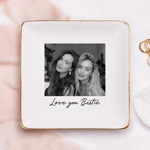 Puede incluir: Una bandeja cuadrada blanca con borde dorado, con una foto en blanco y negro de dos mujeres. La frase "Love you Bestie" est&aacute; escrita debajo. Pendientes de aro dorados con perlas est&aacute;n al lado.