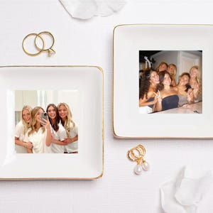 Puede incluir: Dos platos cuadrados blancos con ribete dorado, cada uno con una fotograf&iacute;a. Un plato tiene una foto de cuatro mujeres tom&aacute;ndose una selfie, el otro tiene una foto de un grupo de mujeres. Tambi&eacute;n hay anillos y pendientes dorados.