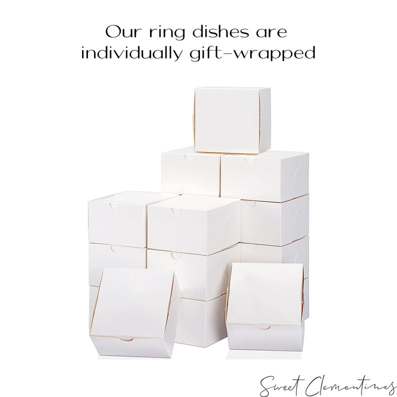 May include: A stack of white ring dishes, individually gift-wrapped in boxes. The boxes are arranged in a pyramid shape, with the top box being the smallest. The text "Our ring dishes are individually gift-wrapped" is visible at the top of the image.