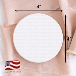May include: A white, 4-inch round coaster with repeating text that reads "sweet clementines co" and "made in california handmade." The coaster is made in the USA and rests on a pink fabric.