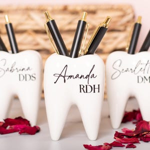 May include: Three white ceramic tooth-shaped pencil holders with black lettering. The holders are personalized with the names Sabrina DDS, Amanda RDH, and Scarlett DMD.