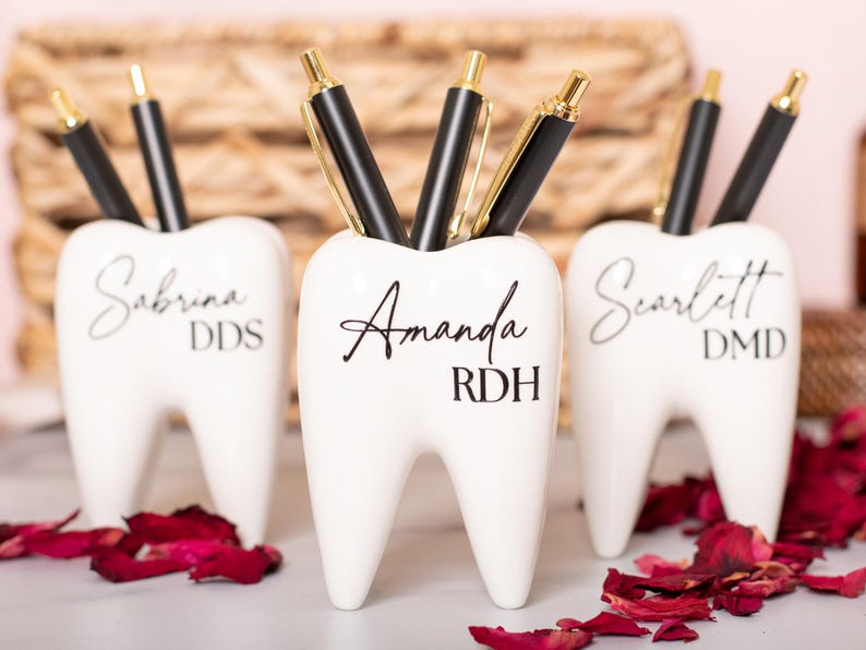 May include: Three white ceramic tooth-shaped pencil holders with black lettering. The holders are personalized with the names Sabrina DDS, Amanda RDH, and Scarlett DMD.