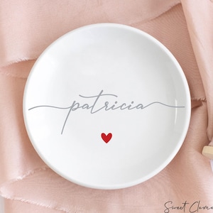 K&ouml;nnte beinhalten: Eine wei&szlig;e Keramik-Schmuckschale mit dem Namen "patricia" in grauer Schrift und einem kleinen roten Herz in der Mitte.