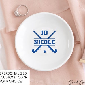 May include: White ceramic ring dish with a blue hockey stick design and the text "10 NICOLE".