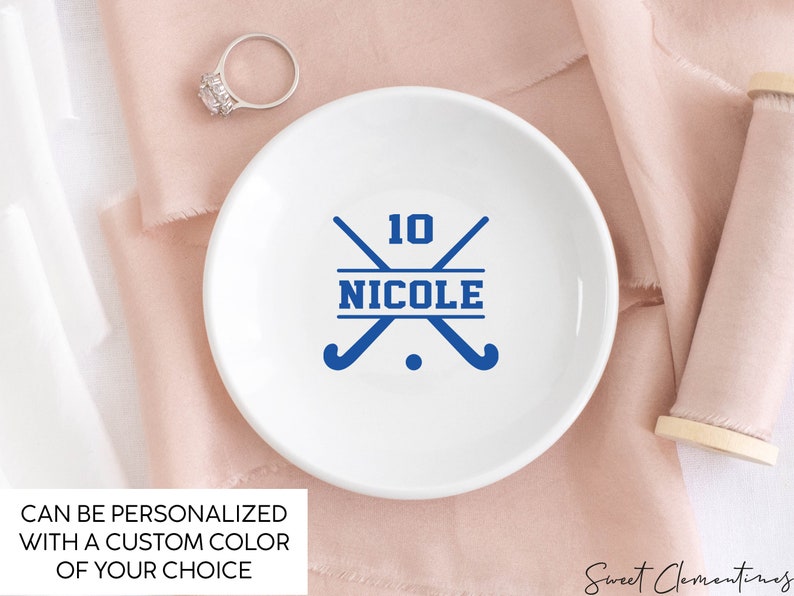 May include: White ceramic ring dish with a blue hockey stick design and the text "10 NICOLE".
