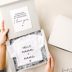 Op de afbeelding: Een witte baby romper met de tekst "HELLO nana + nani" en een klein hartje. De romper zit in een witte cadeaudoos met wit tissuepapier. Een kaart met de tekst "HI NANA & NANI, WE HAVEN'T MET YET BUT I ALREADY KNOW... I love you" ligt op het tissuepapier.