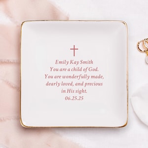 May include: White ceramic trinket dish with a gold rim. The dish has a cross and the text "Emily Kay Smith You are a child of God. You are wonderfully made, dearly loved, and precious in His sight. 06.25.25" in pink.