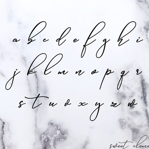 May include: A handwritten alphabet in a cursive font on a white marble background. The letters are written in black ink.