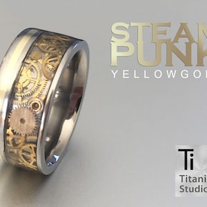 May include: A titanium ring with a gold band and a steampunk design featuring gears and clockwork. The ring is engraved with the words "STEAMPUNK YELLOW GOLD".