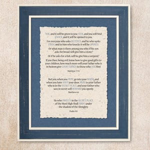 May include: A framed print with a blue background and a white paper insert. The paper insert features a vintage-style font and includes bible verses from Matthew and Psalm 91. The text reads: "Ask, and it will be given to you: Seek, and you will find: Knock, and it will be opened to you. For everyone who asks receives, and he who seeks finds, and to him who knocks it will be opened. Or what man is there among you who, if his son asks for bread, will give him a stone? Or if he asks for a fish, will he give him a serpent? If you then, being evil, know how to give good gifts to your children, how much more will your Father who is in heaven give good things to those who ask Him! Matthew 7:7-8. But you when you pray, go into your room, and when you have shut your door, pray to your Father who is in the secret place; and your Father who sees in secret will reward you openly. Matthew 6:6. He who dwells in the secret place of the Most High shall abide under the shadow of the Almighty. Psalm 91."