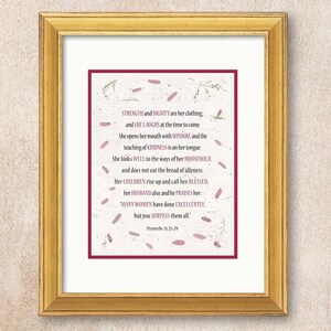 May include: A framed print with a gold-colored frame. The print features a poem with a burgundy border and decorative floral accents. The text includes the words "STRENGTH and DIGNITY" and "Proverbs 31:25-29."