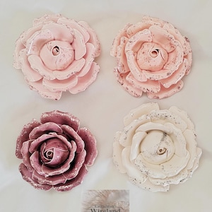Könnte beinhalten: Vier Keramikrosen-Skulpturen in quadratischer Anordnung. Zwei Rosen sind hellrosa mit dunkelrosa Sprenkeln, eine ist tiefmalvenfarben mit silbernen Glitzerakzenten und eine ist cremeweiß mit silbernem Glitzer. Der Text lautet KatTheMyths Wireland.