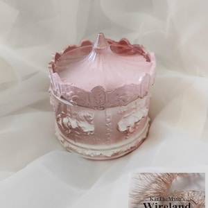 May include: A pink carousel-shaped trinket box with a detailed design. The box features a domed top and decorative carvings, with a white and pink colour scheme. The box is sitting on a white surface. The text "KatTheMyth's Wireland" is in the bottom right corner.