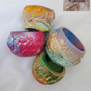 May include: Four small, round, textured bowls with embossed designs. One is yellow and orange with birds, one is bright pink and blue, one is blue, gold, and green with mountain motifs, and one is green and gold with floral patterns. KatTheMyth's Wireland.