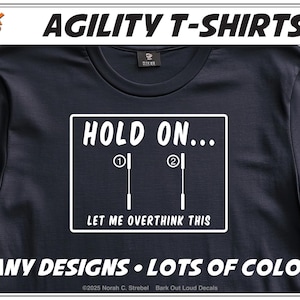 May include: Black agility t-shirt with white text. The shirt features the phrase "HOLD ON... LET ME OVERTHINK THIS" inside a white rectangle. The top of the shirt reads "AGILITY T-SHIRTS". The bottom of the shirt reads "MANY DESIGNS • LOTS OF COLORS".