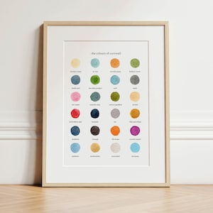 May include: Framed print titled "the colours of cornwall" featuring a grid of colorful circles. Each circle represents a color with a corresponding name, such as "clotted cream" and "strawberry jam". The frame is light wood, and the print is on white paper.