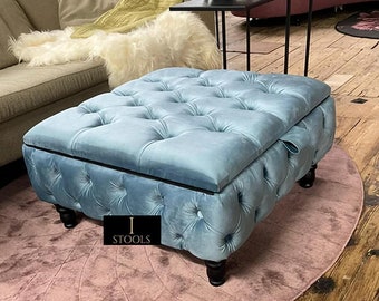 May include: A light blue tufted storage ottoman with a black trim and wooden legs. The ottoman is sitting on a pink rug.