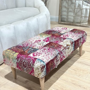 May include: A rectangular ottoman with a patchwork design featuring a variety of colours and patterns, including pink, teal, gold, and white. The ottoman has four wooden legs.