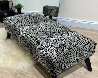 May include: A black and white patterned footstool with black wooden legs. The footstool is upholstered in a fabric with a small, repeating pattern of black and white circles.