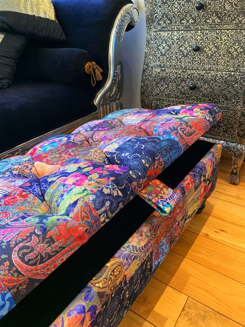 Op de afbeelding: Een kleurrijke, gepatroneerde opbergottoman met een gestoffeerde bovenkant en een zwart interieur. De ottoman is open, waardoor de opbergruimte zichtbaar is.