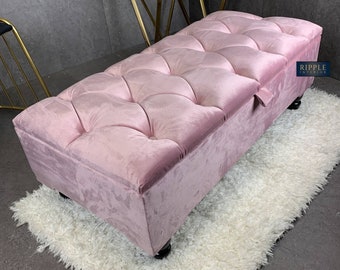 以下が含まれることがあります： ピンクのベルベット製の収納オットマンで、ステッチが施されたデザインと木製の脚が付いています。オットマンは白いふわふわのラグの上に置かれています。