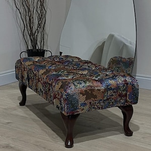 May include: A rectangular ottoman with a mosaic pattern in various colours. It has dark wooden, curved legs and a tufted top. The design is vintage, with the legs measuring approximately 40 cm in height.