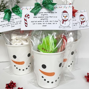 Può includere: Tazze bianche a tema pupazzo di neve riempite con marshmallow, un sapone verde a forma di albero e bastoncini di zucchero. Ogni tazza è confezionata in un sacchetto trasparente e sormontata da una carta con la scritta "winter weather may be frightful". Le tazze sono decorate con punti neri e sorrisi arancioni.