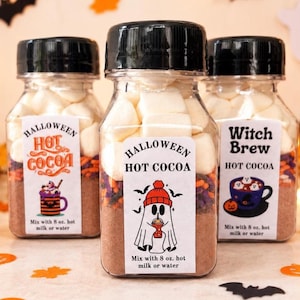 May include: Three clear plastic bottles filled with layers of hot cocoa mix, colorful sprinkles, and white marshmallows. Each bottle has a black cap and a white label featuring Halloween-themed graphics and the text "Halloween Hot Cocoa" or "Witch Brew" with instructions to mix with 8 oz. hot milk or water.