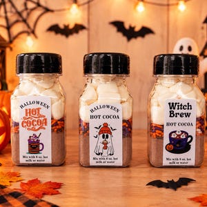May include: Three clear plastic bottles filled with layers of hot cocoa mix, colorful sprinkles, and white marshmallows. Each bottle has a black cap and a white label with Halloween-themed graphics and text, including instructions to mix with 8 oz. hot milk or water.