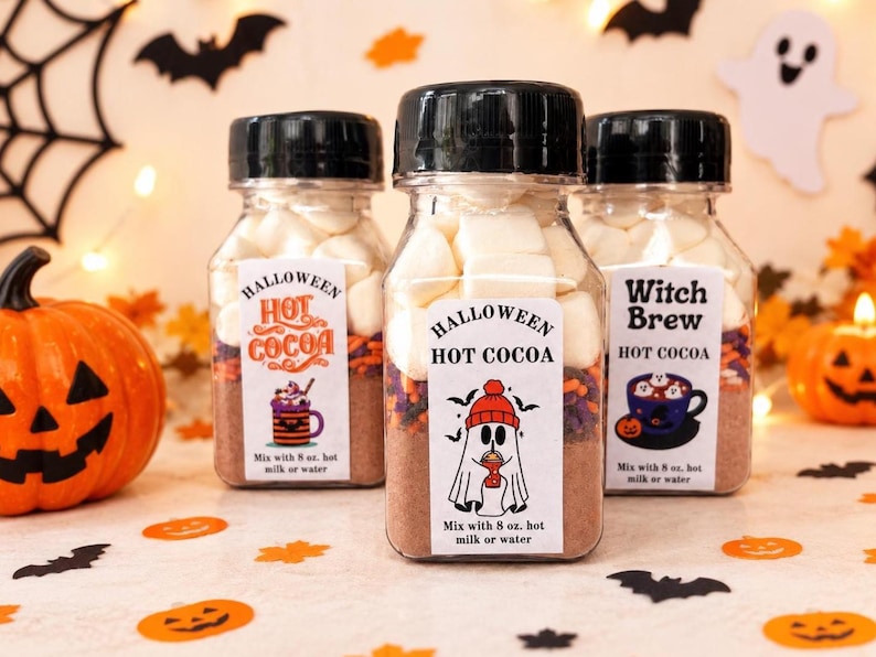 May include: Three clear plastic bottles filled with layers of hot cocoa mix, colorful sprinkles, and white marshmallows. Each bottle has a black cap and a white label featuring Halloween-themed graphics and the text "Halloween Hot Cocoa" or "Witch Brew" with instructions to mix with 8 oz. hot milk or water.