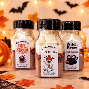May include: Three clear plastic jars filled with hot cocoa mix, colorful sprinkles, and white marshmallows. Each jar has a black screw-top lid and a white label featuring Halloween-themed graphics and text that reads Mix with 8 oz. hot milk or water.