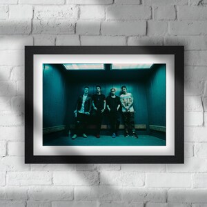 May include: Four men standing in an elevator, wearing casual clothing. The elevator has a teal green interior and the men are looking at the camera.