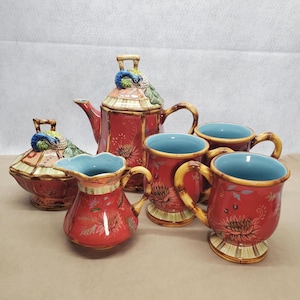 May include: A red and gold tea set with a peacock design. The set includes a teapot, creamer, sugar bowl, and four mugs.