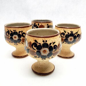 May include: Set of four small ceramic cups with a footed base. The cups are decorated with a floral pattern in shades of brown, black, and white.