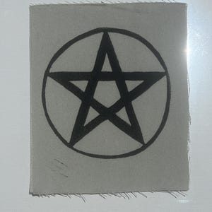 May include: A rectangular light gray fabric patch featuring a black screen-printed pentagram design centered on the material. The edges of the patch are unfinished and frayed, showing the woven texture of the textile base with a clear black ink.