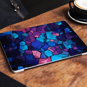 May include: A laptop computer with a colorful geometric design on the cover. The design features a variety of blue, purple, and pink squares and rectangles.