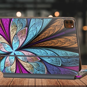 Può includere: Una custodia per laptop con motivo blu, viola e oro con tastiera integrata. La custodia presenta un design floreale con dettagli intricati.