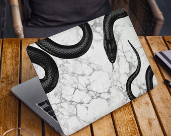 May include: A laptop computer with a white marble design and black snake illustrations. The laptop is closed and sitting on a wooden surface.