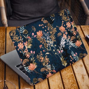 以下が含まれることがあります： 蓋に花柄のデザインが施されたラップトップコンピューター。デザインは、濃い青色の背景に、ピンク、オレンジ、イエロー、グリーンの色合いのさまざまな花や葉が描かれています。