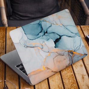 Könnte beinhalten: Ein Laptop mit einem blauen und goldenen Marmormuster auf dem Deckel. Der Laptop ist geöffnet und die Tastatur ist sichtbar.