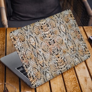 K&ouml;nnte beinhalten: Ein Laptop mit einem braunen und schwarzen Schlangenhautmuster auf dem Deckel. Der Laptop steht auf einem Holztisch.