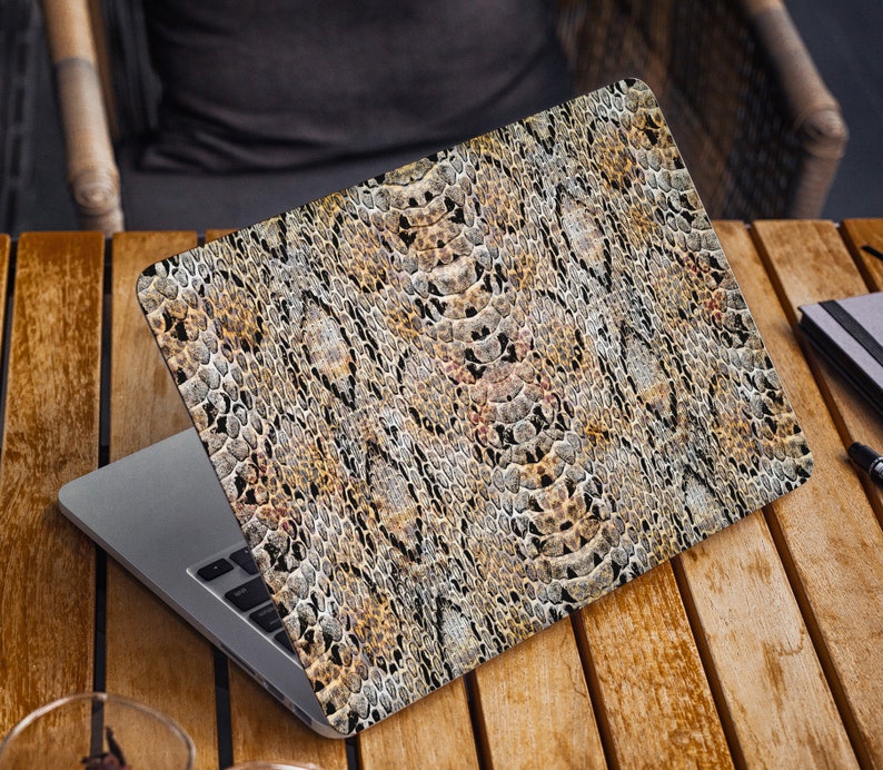 K&ouml;nnte beinhalten: Ein Laptop mit einem braunen und schwarzen Schlangenhautmuster auf dem Deckel. Der Laptop steht auf einem Holztisch.