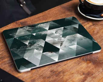 May include: A laptop computer with a geometric design featuring a dark green and white pattern of waves crashing on a beach. The laptop is on a wooden surface.