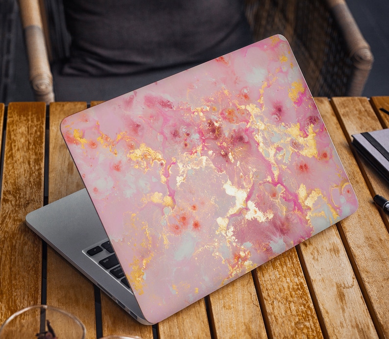 Pode incluir: Um computador port&aacute;til com um design de m&aacute;rmore rosa e dourado na tampa. O laptop est&aacute; aberto e o teclado &eacute; vis&iacute;vel.