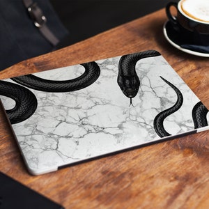May include: A laptop skin with a white marble pattern and black snake designs.