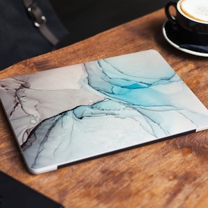 May include: A laptop computer with a blue and grey abstract design on the cover. The design resembles flowing watercolours.